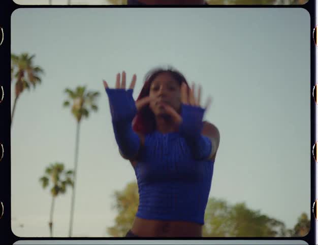 Young woman with red hair dances in front of palm trees caught on vintage film