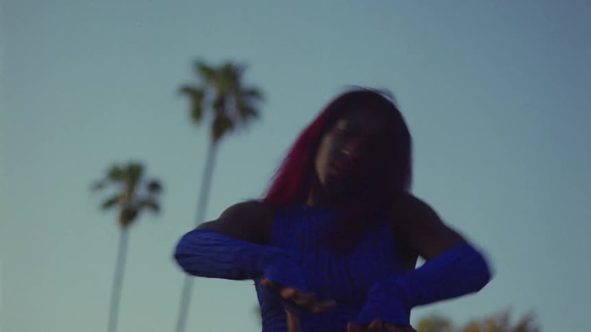 Young woman with red hair dances in front of palm trees caught on vintage film