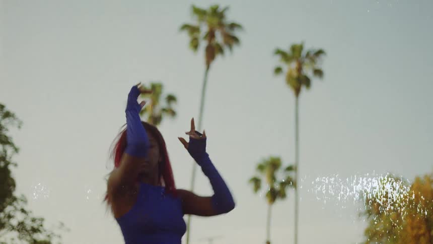 Woman with red hair blue top and sports pants dances on lawn in public park