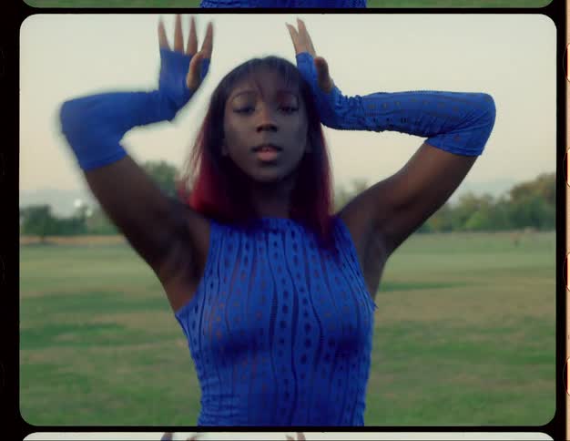 Black woman wearing long blue gloves and a blue dance costume dances while in a field
