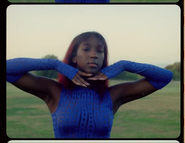 A teenage girl wearing a blue outfit is dancing outside in a field