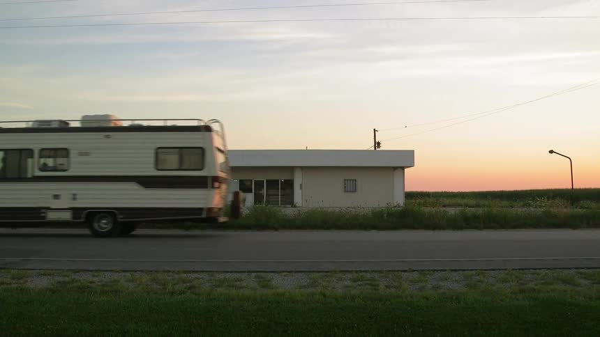 An rv drives past a white building at sunset