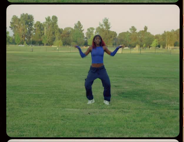 Woman with red hair blue top and sports pants dances on lawn in public park