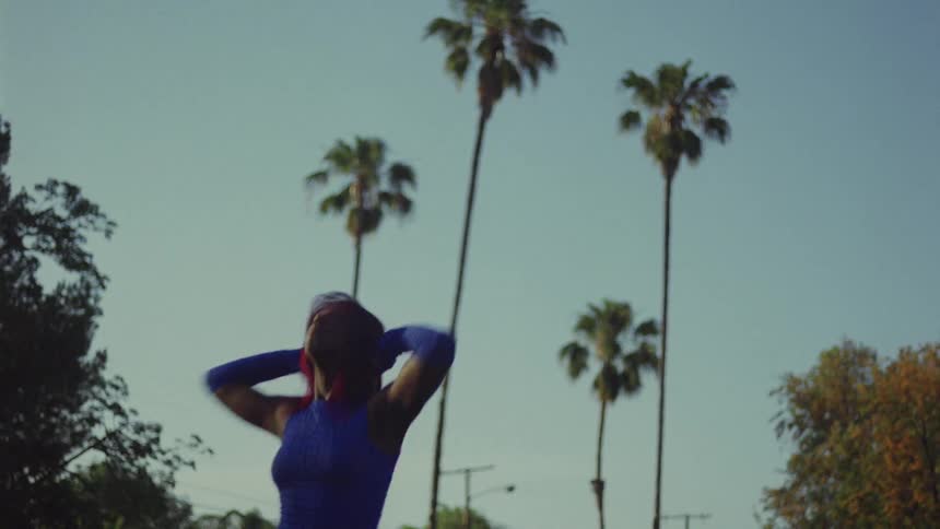 Woman with red hair blue top and sports pants dances on lawn in public park