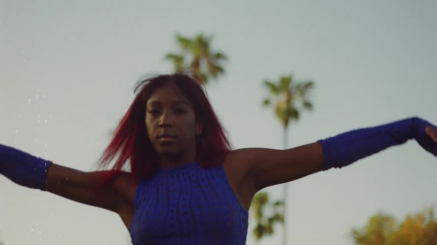 A teenage girl wearing a blue outfit is outside dancing on a neighborhood street