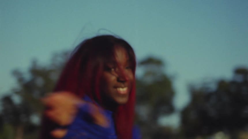 Woman with red hair blue top and sports pants dances on lawn in public park