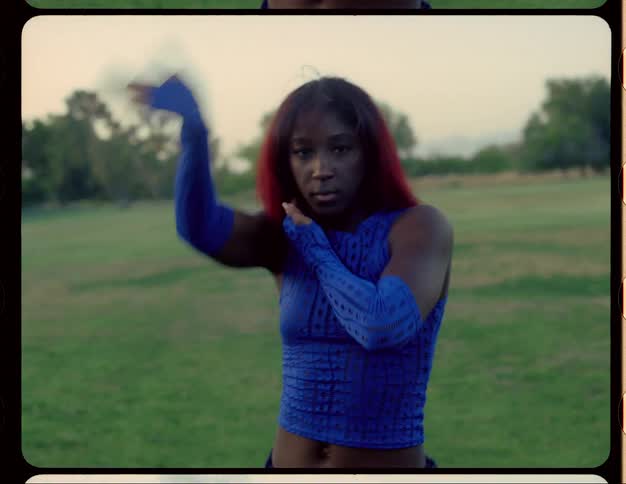 Woman with red hair blue top and sports pants dances on lawn in public park