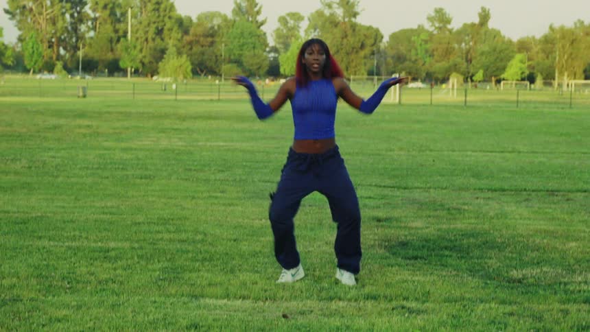 Black woman dancing alone in the middle of the grass field in a public park on a sunny day