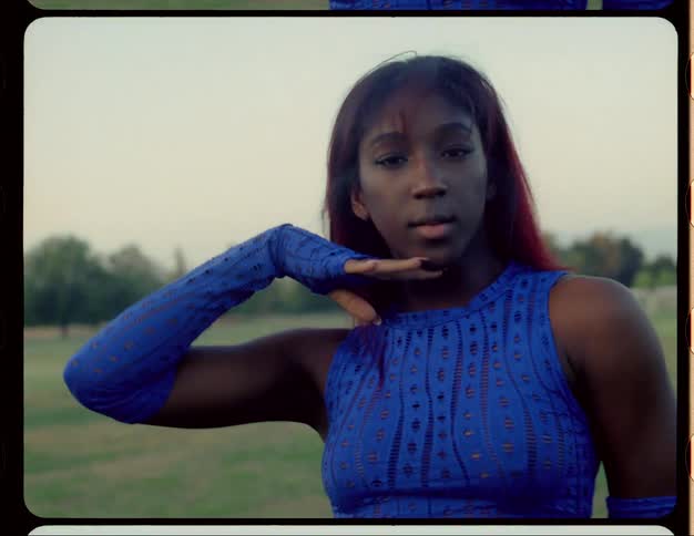 Woman with red hair blue top and sports pants dances on lawn in public park