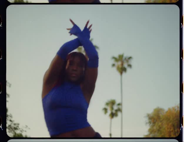 Young woman with red hair dances in front of palm trees caught on vintage film