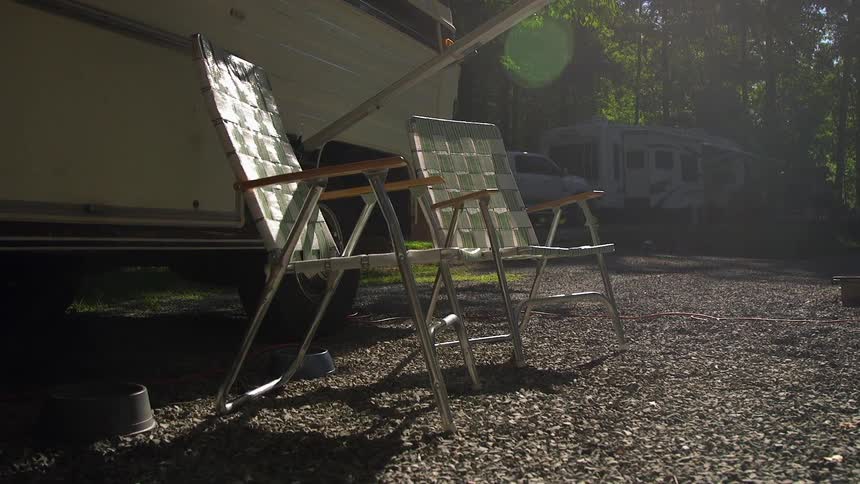Two lawn chairs are on a field with recreational vehicles