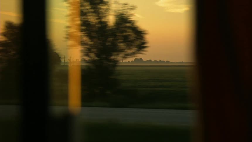 A moving vehicle has a view of a large green field at sunset