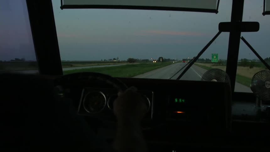 A vehicle drives on a rural road at sunset