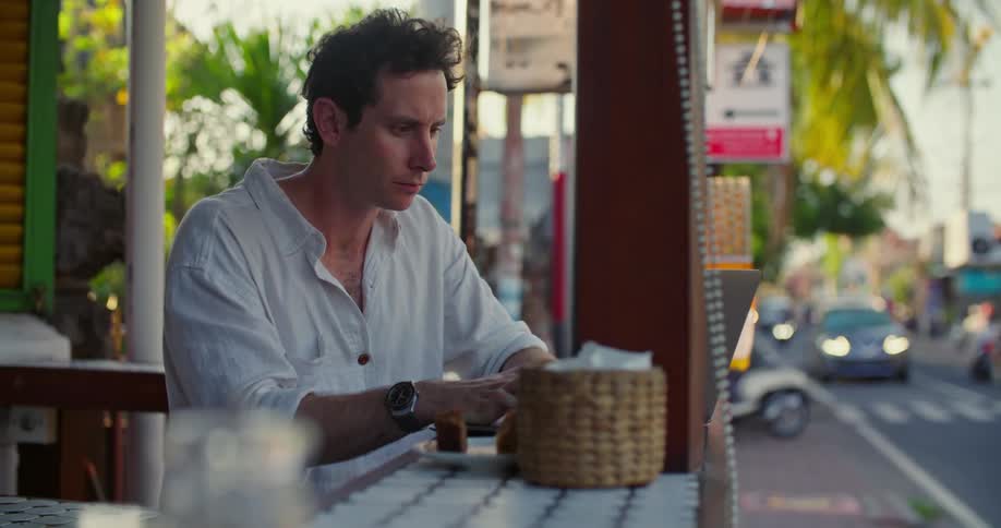 Traffic passes by a man eating lunch on the patio of a restaurant