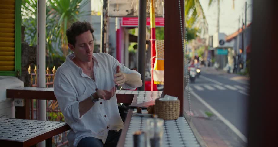 A man works on his laptop at a restaurant as scooter traffic passes by