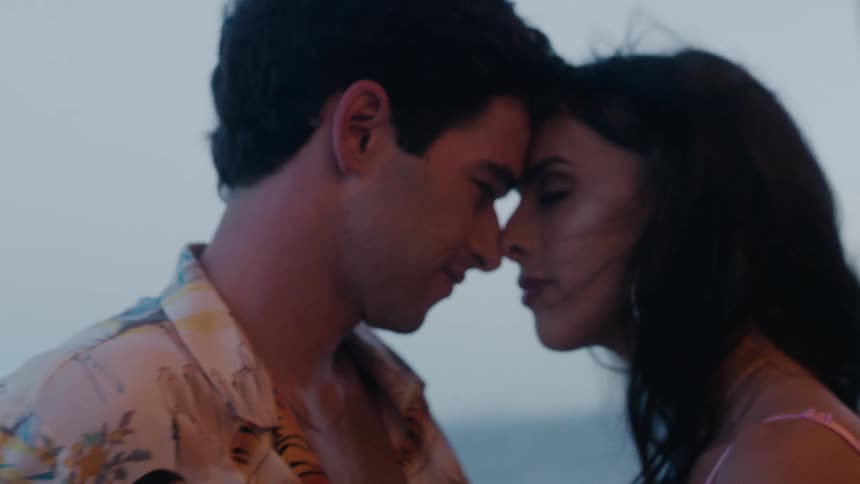 A man and woman lean in to kiss while standing outside