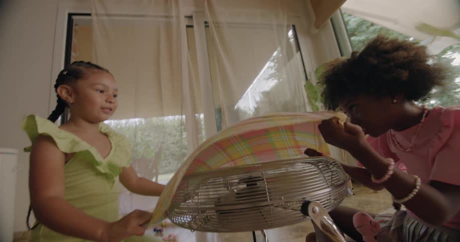 Two girls laugh as the fabric they hold over a fan flies away