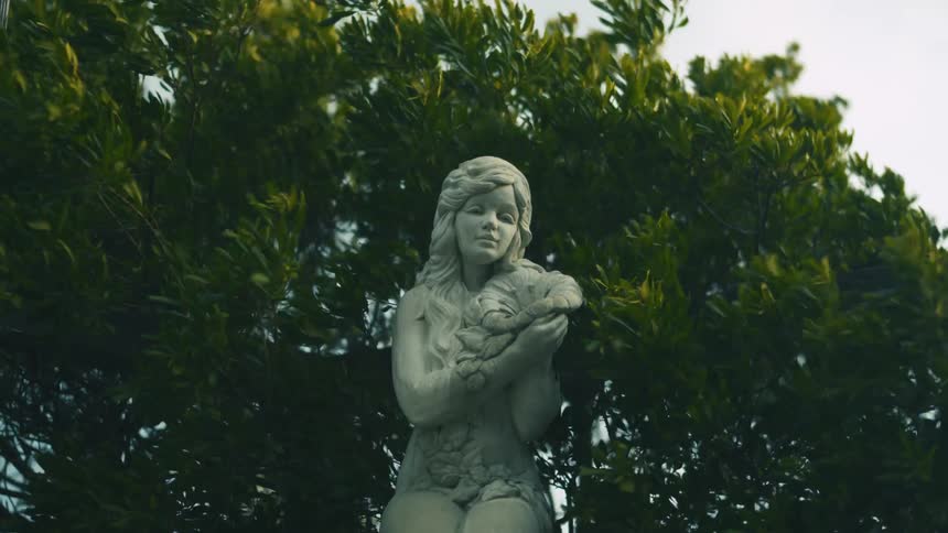 Branches blow in the wind around a statue of a woman