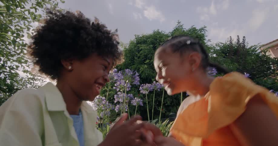 Two young female friends laughs together in yard near flowers