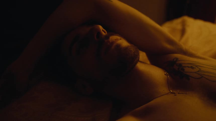 Man lies in shadowy room with his arm over his head