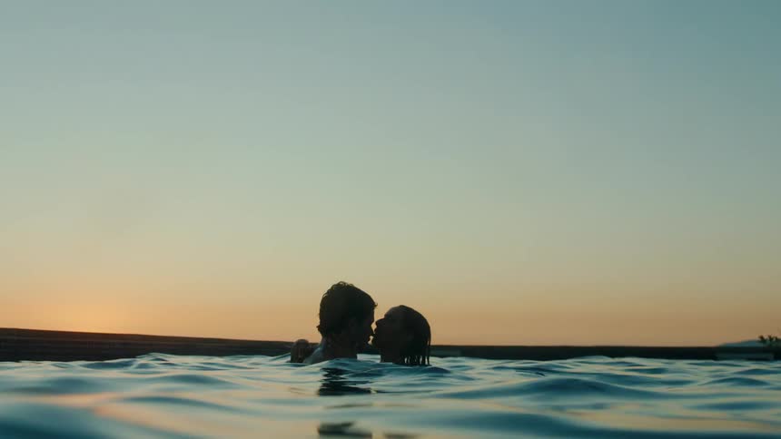 A man and a woman are standing in neck deep water kissing and he suddenly throws her underwater