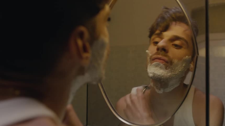 A man leans into a mirror while shaving