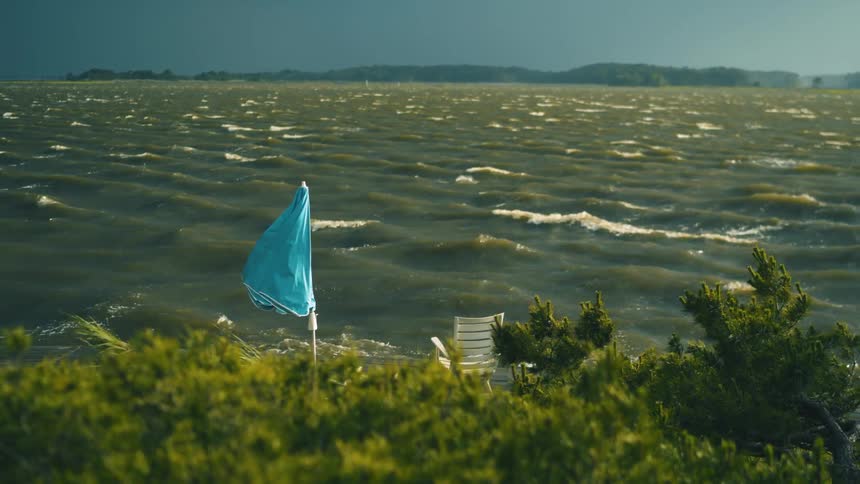 Hurricane winds blow across a bay as an umbrella flaps