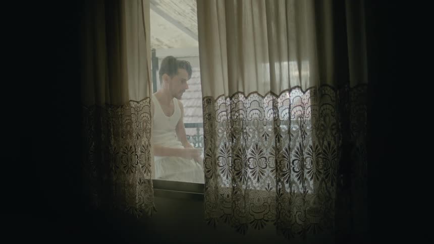 A man can be seen through a window standing on the porch smoking a cigarette