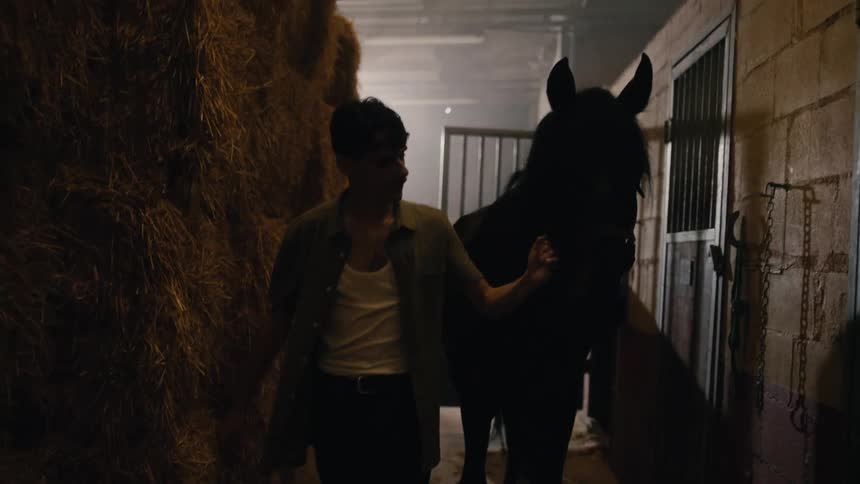 A man pets his horse while leading it down a hallway at the stable