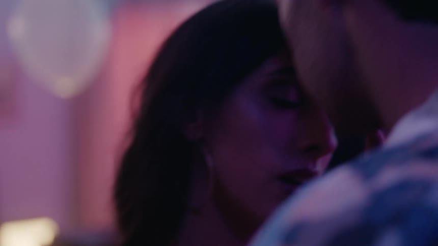 A couple lean in to kiss while dancing at a club