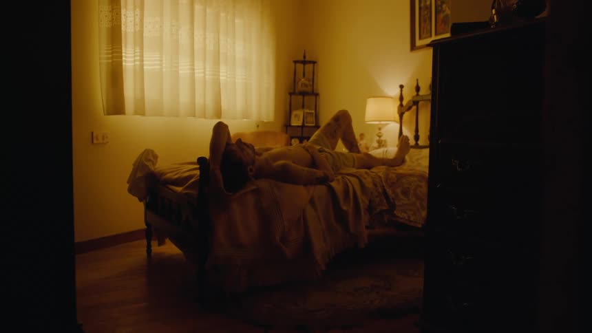 A man is in his bedroom lying on the bed and a lamp is on