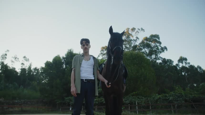 Man stands holding rein of horse in corral
