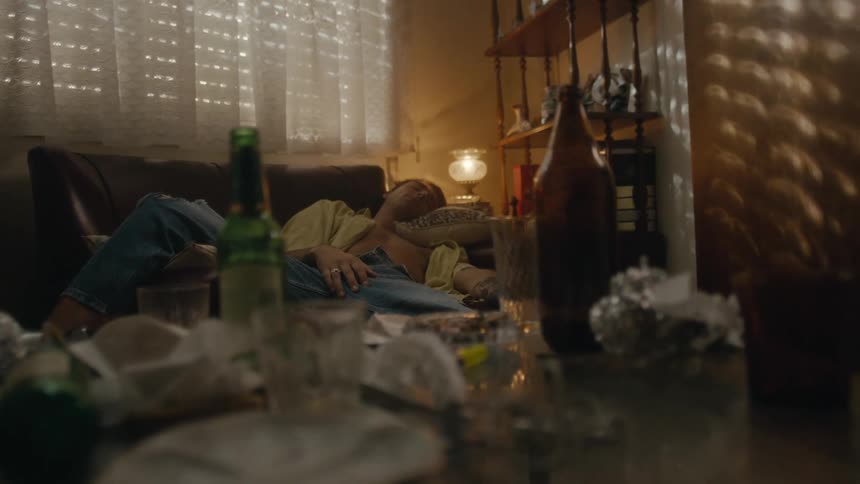 A man is passed out on a couch and there are beer bottles and food wrappers on a table