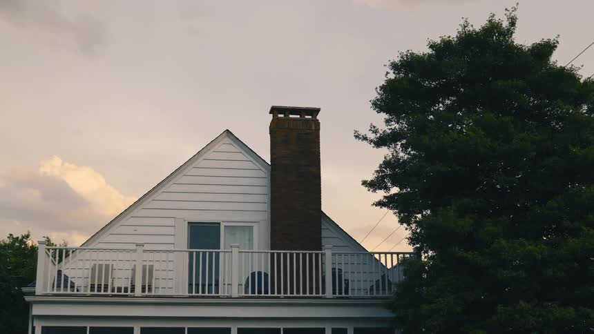 Exterior view of house with chimney next to tree at dusk