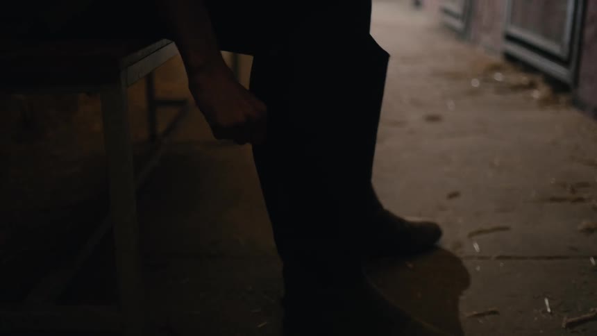 A man puts on his riding boots in a horse stable