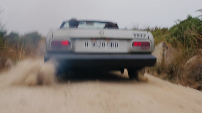 Convertible speeds down dirt road kicking up dust