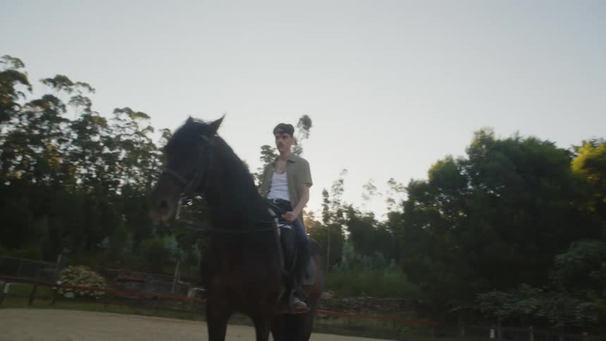 A man rides his horse in a fenced in stable