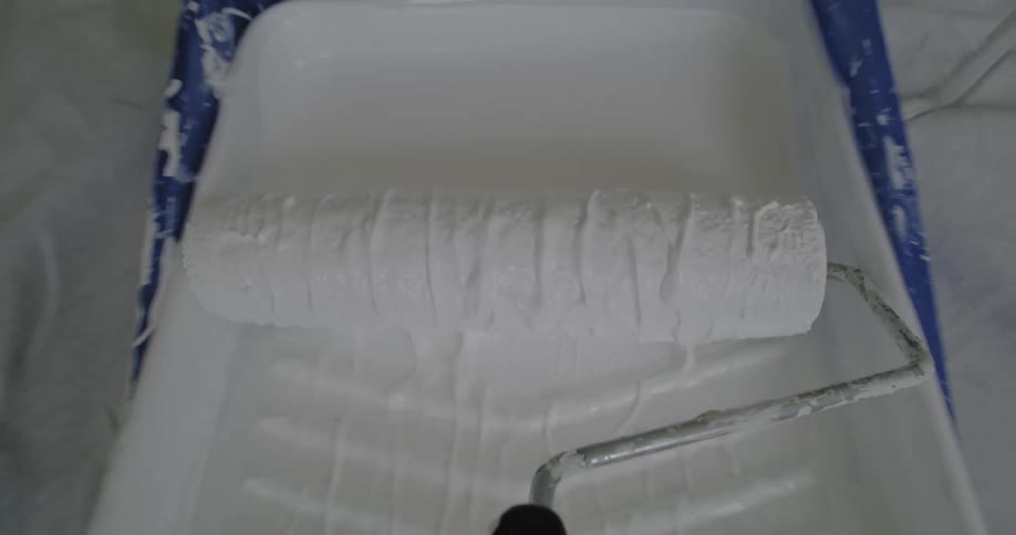 Someone is moving a roller across a tray filled with white paint