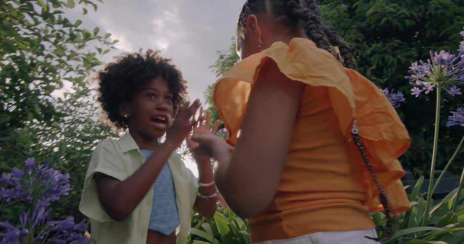 Two girls with curly hair and ponytail play together in the garden