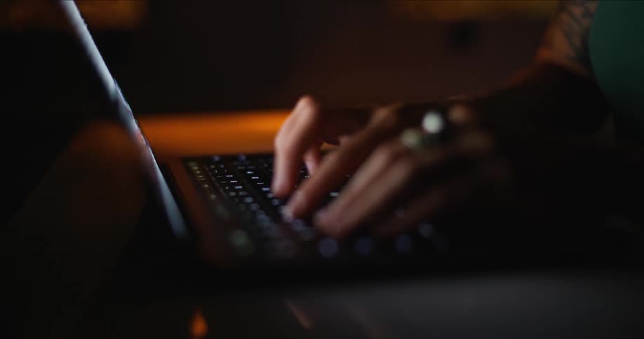 Woman types on laptop in dark room