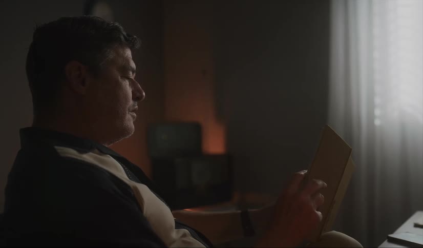 Middle aged man sitting in cair reads a book and looks at his wristwatch