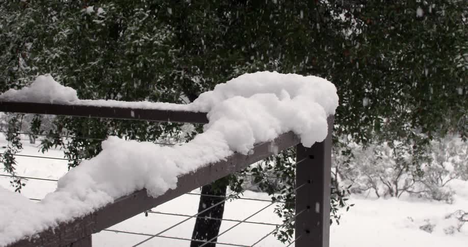 It is snowing on this porch near some trees