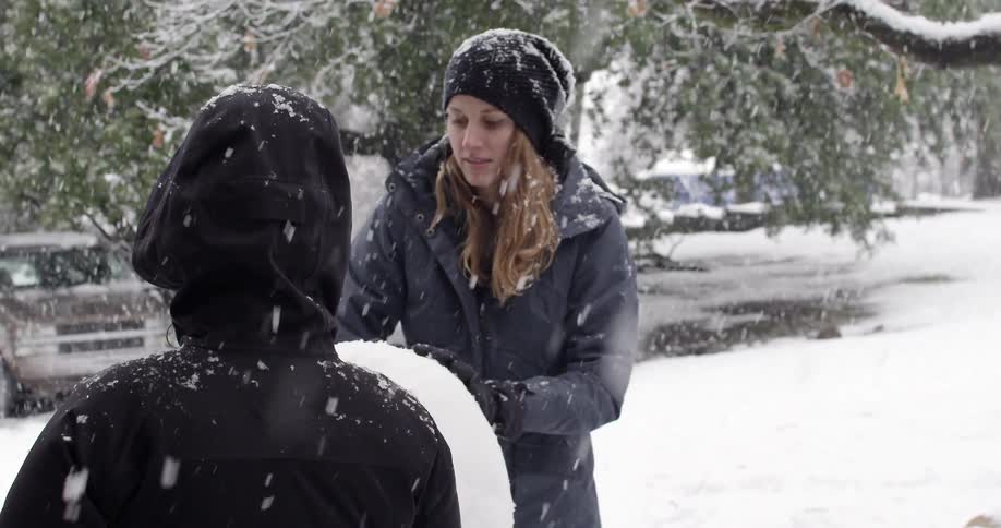 Snow falls while a woman builds a snowman