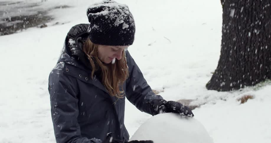 A woman is building a snowman as it snows