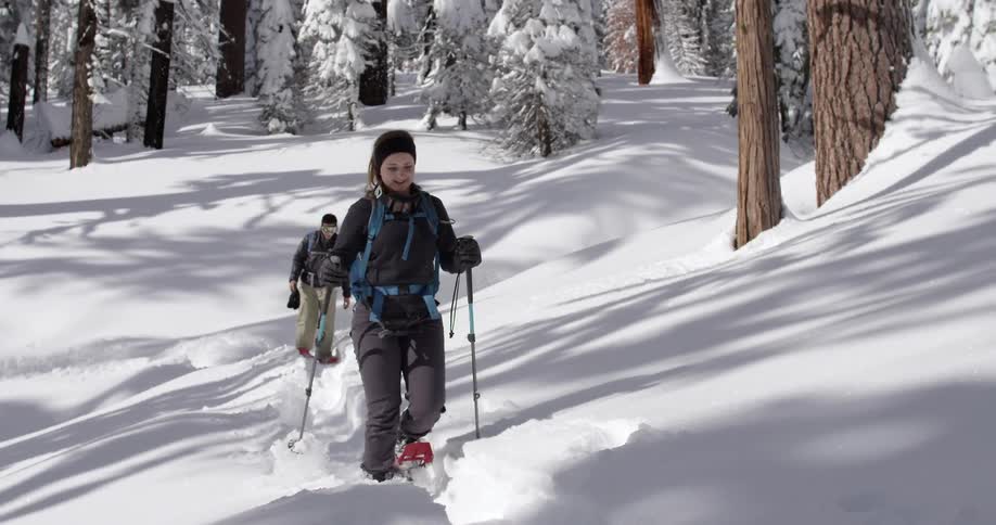 A woman is hiking as a man follows behind in the snow