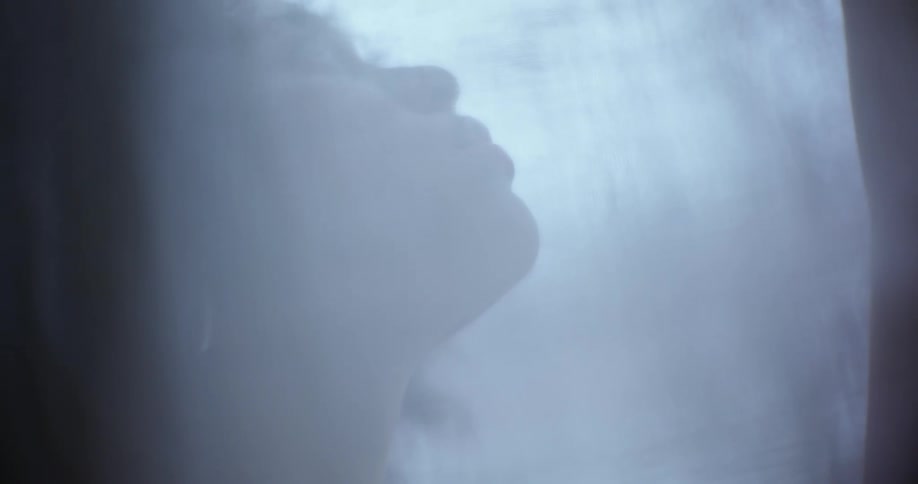 A woman leans her head back with her eyes closed while standing behind a curtain