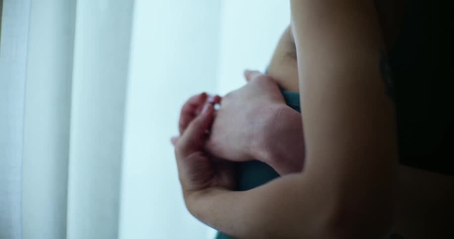 Close up of the hands of a couple hugging and holding hands near a window