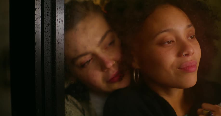 Woman standing in front of a window at home receives a hug from her couple from behind