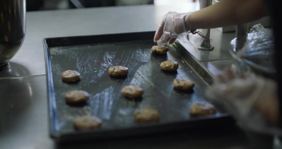 A baker places balls of dough on a greased baking pan on a kitchen counter