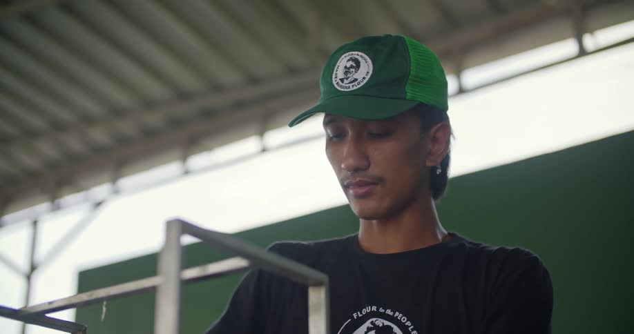 A young man wearing a hat and t shirt with a flour company logo on it at work